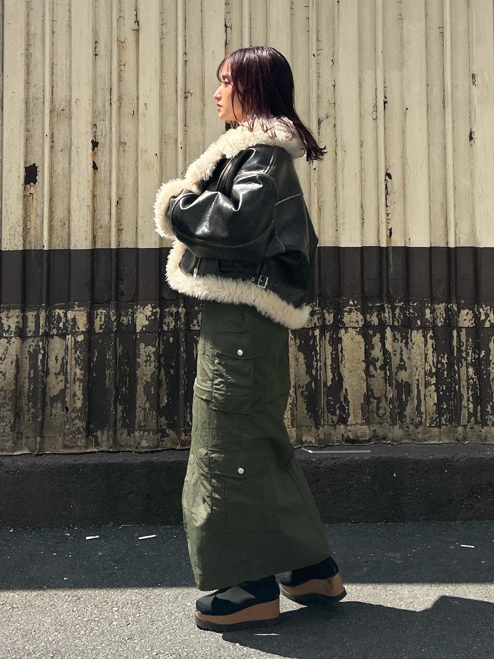 ブラウン系のムートンコート、グレー系のニット/セーター、グリーン系のスカートを着用したレディースの秋コーディネートの3枚目の写真