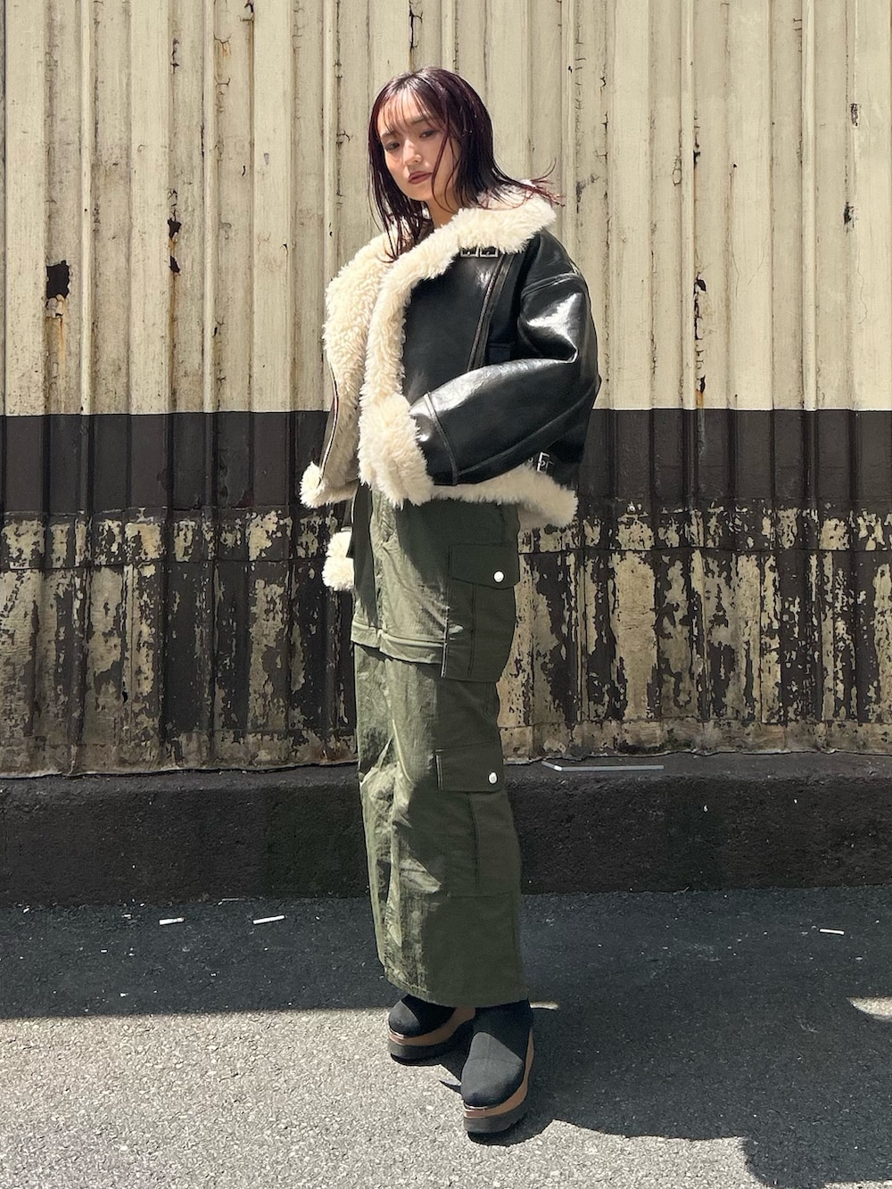 ブラウン系のムートンコート、グレー系のニット/セーター、グリーン系のスカートを着用したレディースの秋コーディネートの2枚目の写真