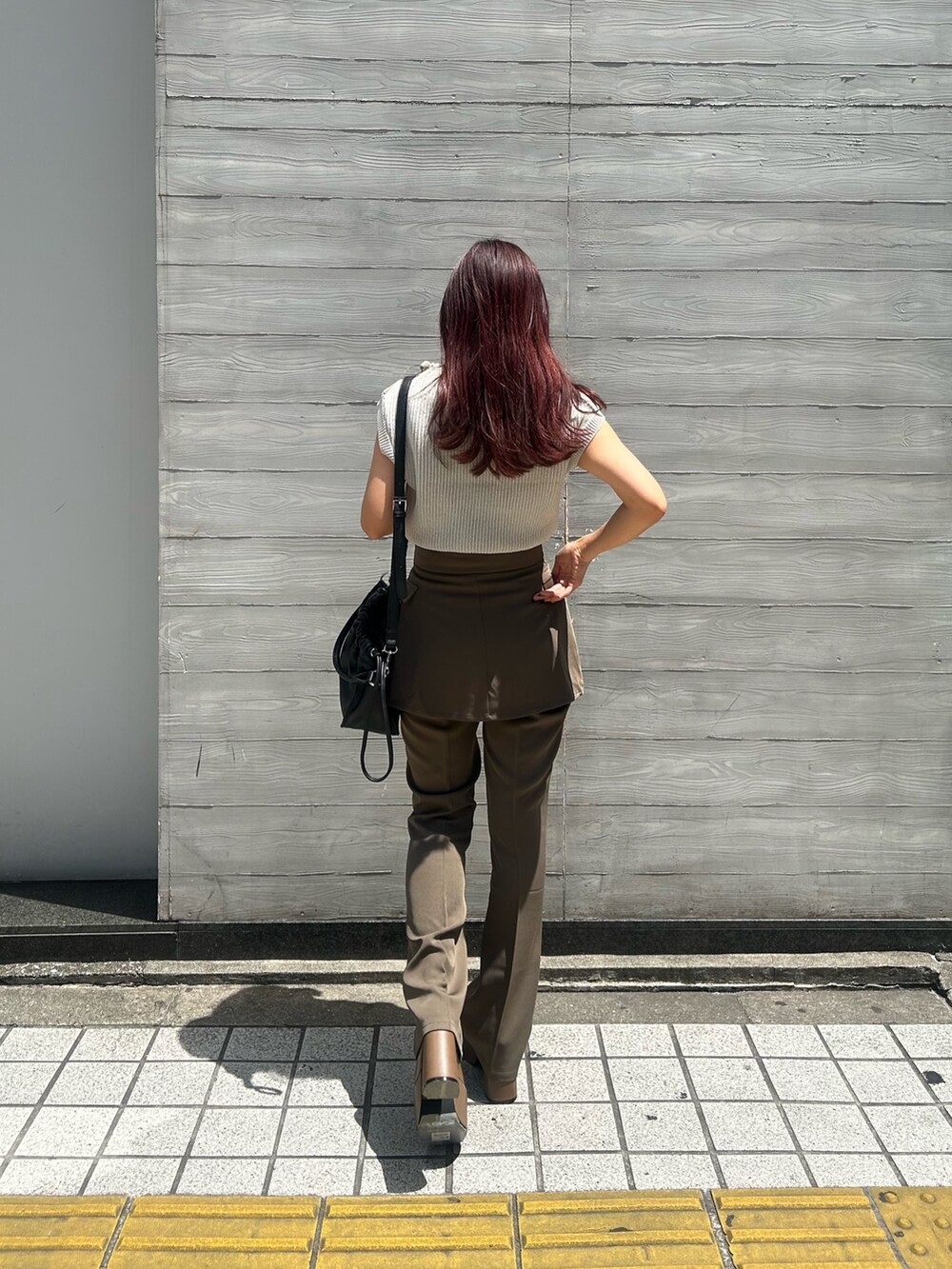 ブラウン系のブーツ、ブラウン系のスラックス、ブラック系のハンドバッグを着用したレディースの夏コーディネートの2枚目の写真