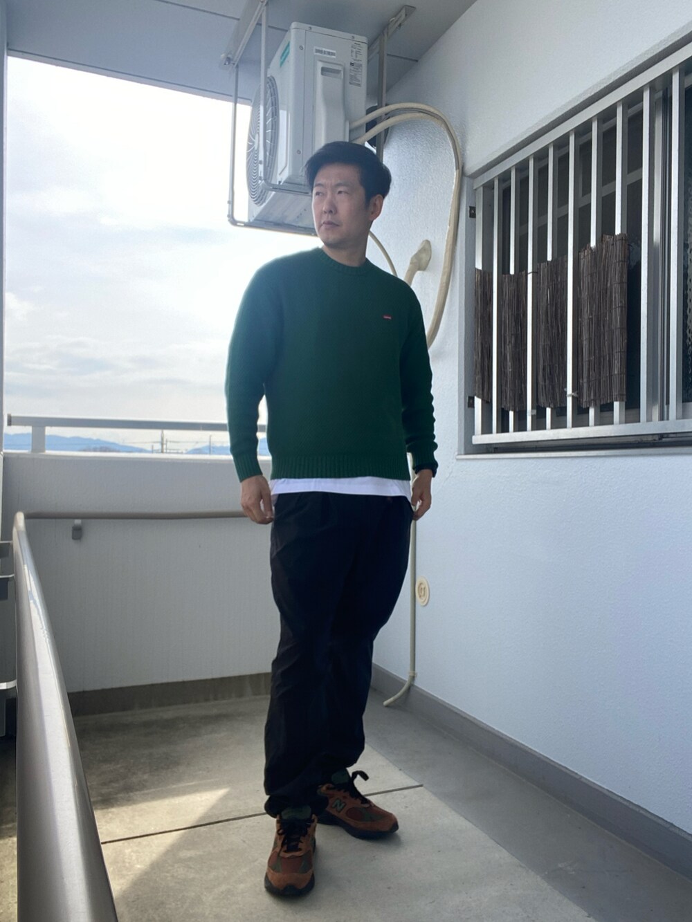 グリーン系のニット/セーター、ベージュ系のダウンベスト、ブラック系のパンツを着用したメンズの春コーディネートの2枚目の写真