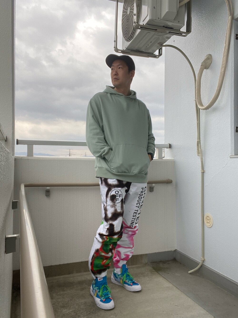 グリーン系のパーカー、ホワイト系のその他パンツ、ブルー系のスニーカーを着用したメンズの春コーディネートの2枚目の写真