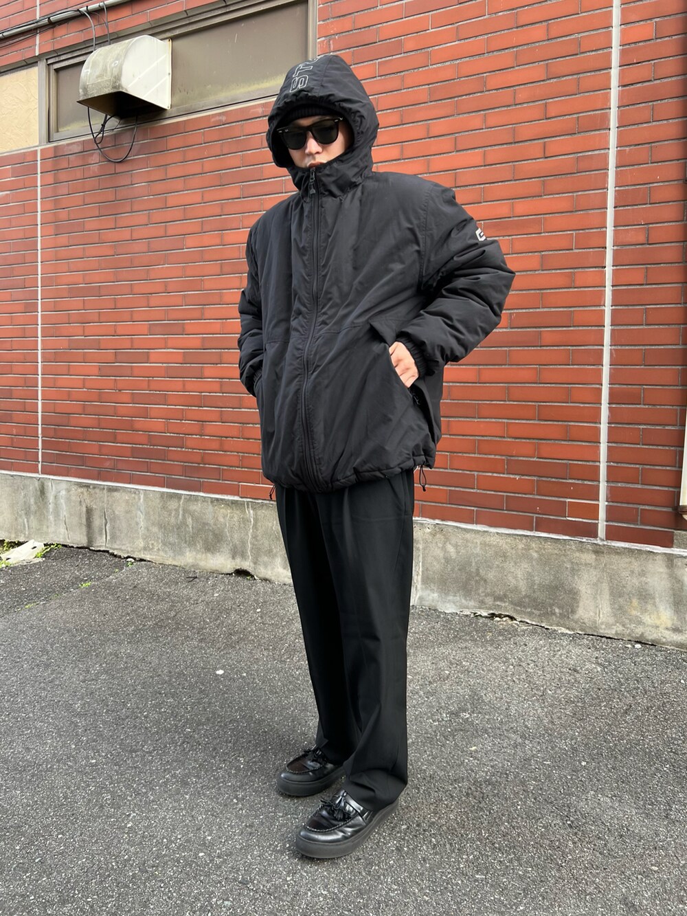 ブラック系のダウンジャケット/コート、ブラック系のその他パンツ、ブラウン系のサングラスを着用したメンズの秋コーディネートの2枚目の写真