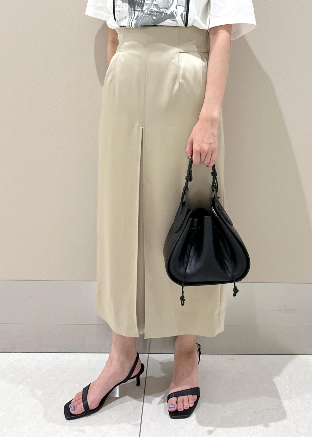 ブラック系のハンドバッグ、ブラック系のサンダル、ベージュ系のスカートを着用したレディースの夏コーディネートの8枚目の写真