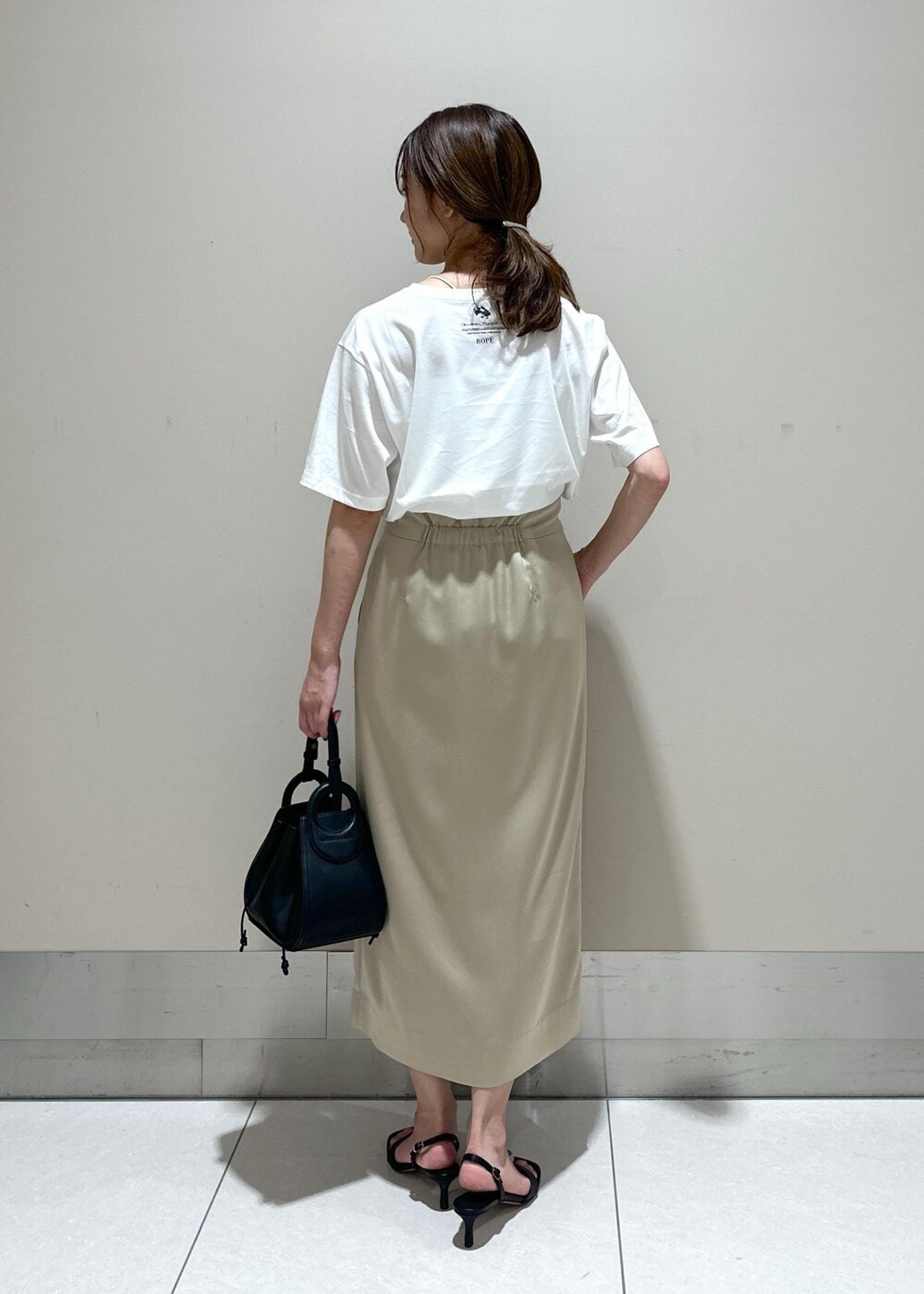 ブラック系のハンドバッグ、ブラック系のサンダル、ベージュ系のスカートを着用したレディースの夏コーディネートの3枚目の写真