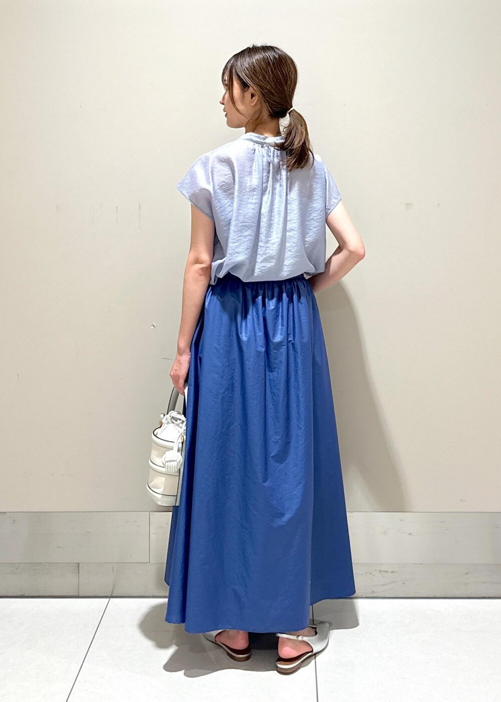 ホワイト系のハンドバッグ、シルバー系のパンプス、ブルー系のシャツ/ブラウスを着用したレディースの夏コーディネートの3枚目の写真