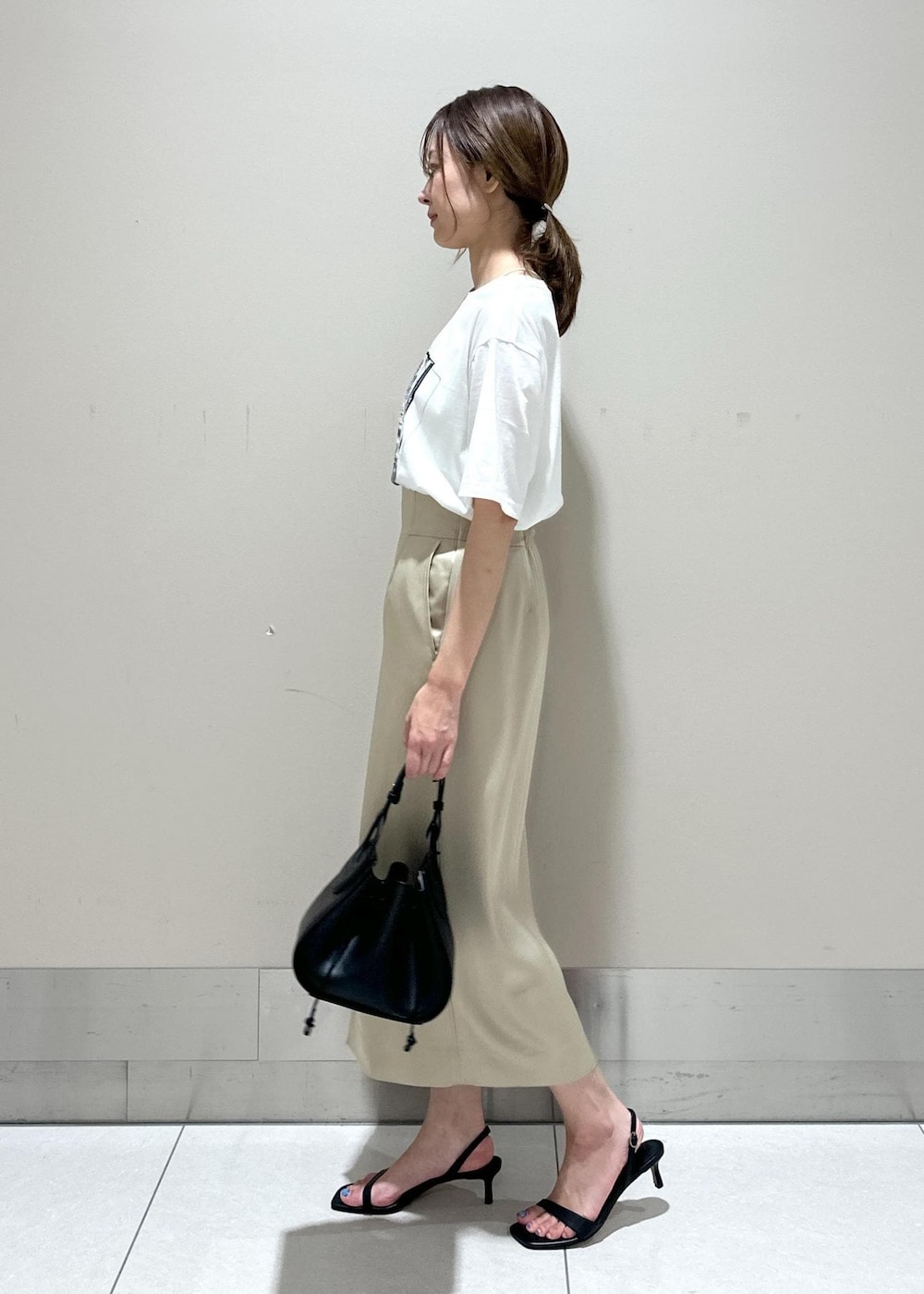 ブラック系のハンドバッグ、ブラック系のサンダル、ベージュ系のスカートを着用したレディースの夏コーディネートの2枚目の写真