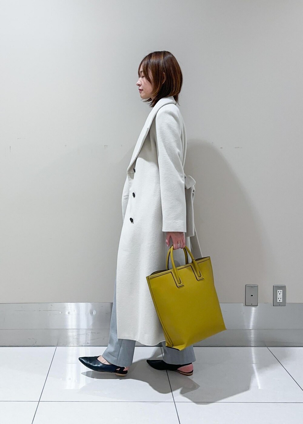 オレンジ系のハンドバッグ、ホワイト系のチェスターコート、グレー系のその他パンツを着用したレディースの秋コーディネートの2枚目の写真