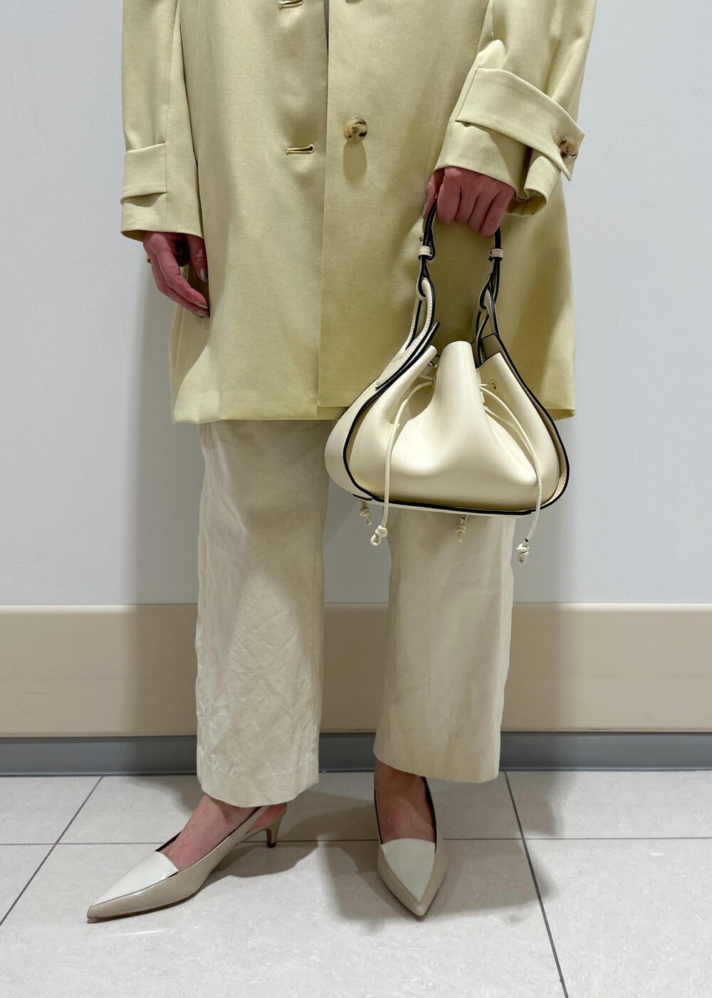 ホワイト系のハンドバッグ、ベージュ系のステンカラーコート、ホワイト系のその他パンツを着用したレディースの春コーディネートの7枚目の写真
