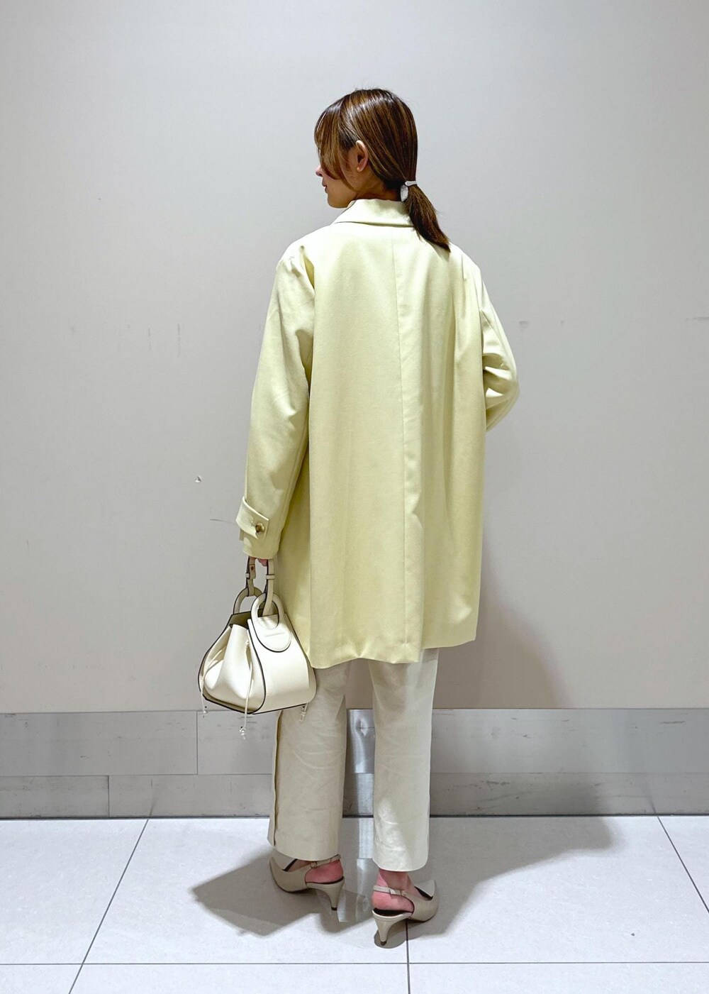 ホワイト系のハンドバッグ、ベージュ系のステンカラーコート、ホワイト系のその他パンツを着用したレディースの春コーディネートの3枚目の写真