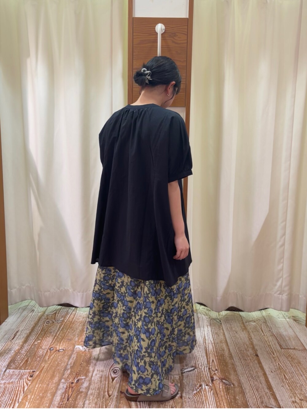 ブラック系のチュニック、イエロー系のスカート、ベージュ系のサンダルを着用したレディースの夏コーディネートの2枚目の写真