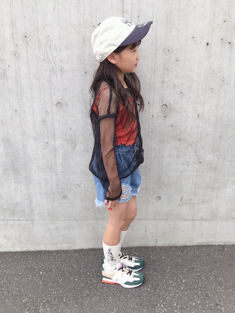 オレンジ系のキャミソール、グリーン系のスニーカー、ホワイト系のキャップを着用したキッズの夏コーディネートの2枚目の写真