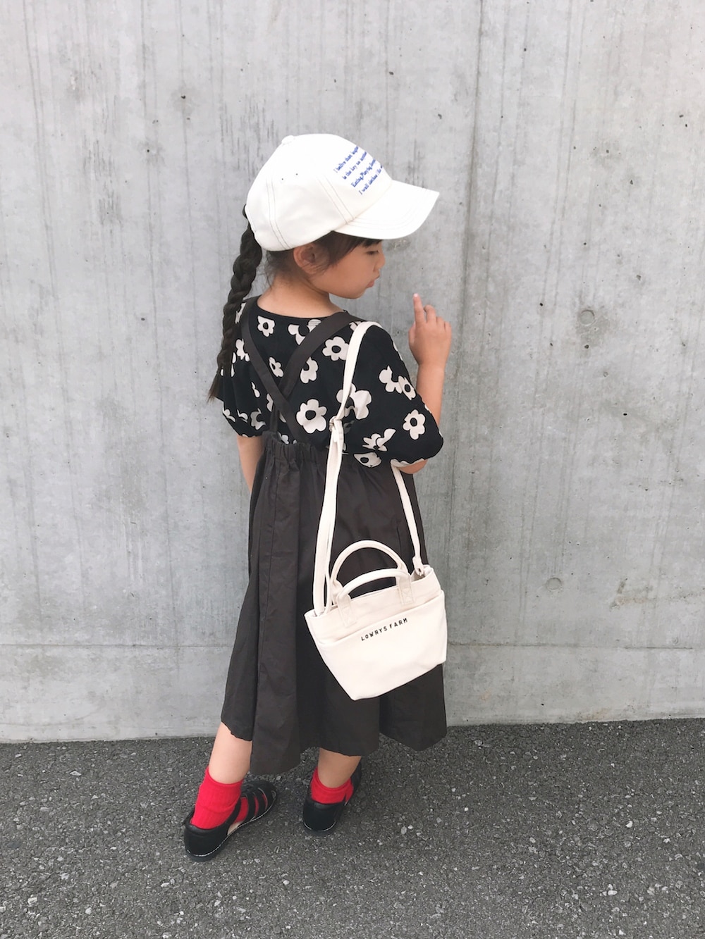 ホワイト系のショルダーバッグ、ブラック系のサンダル、グレー系のジャンパースカートを着用したキッズの夏コーディネートの3枚目の写真