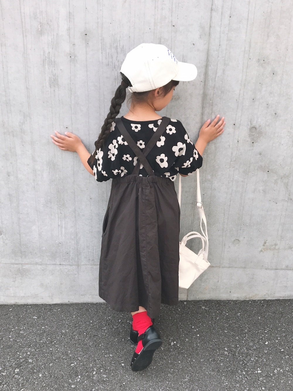 ホワイト系のショルダーバッグ、ブラック系のサンダル、グレー系のジャンパースカートを着用したキッズの夏コーディネートの5枚目の写真