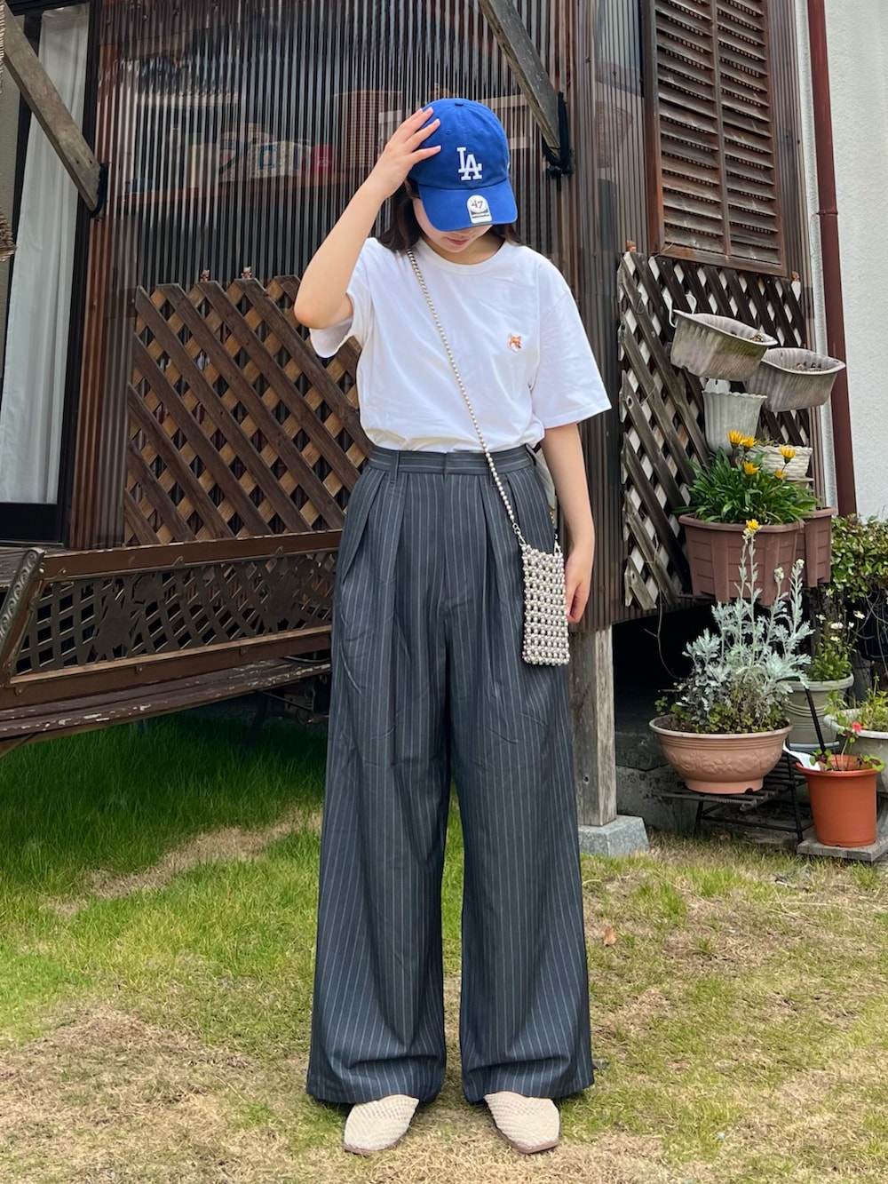 グレー系のスラックス、ホワイト系のスリッポン、シルバー系のショルダーバッグを着用したレディースの夏コーディネートの2枚目の写真