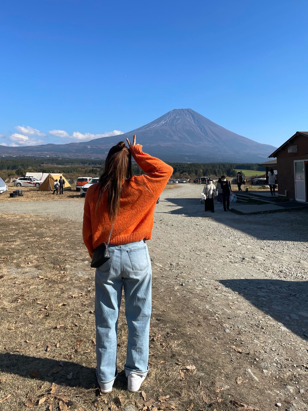 オレンジ系のニット/セーター、ホワイト系のスニーカー、ブラック系のショルダーバッグを着用したレディースの秋コーディネートの2枚目の写真