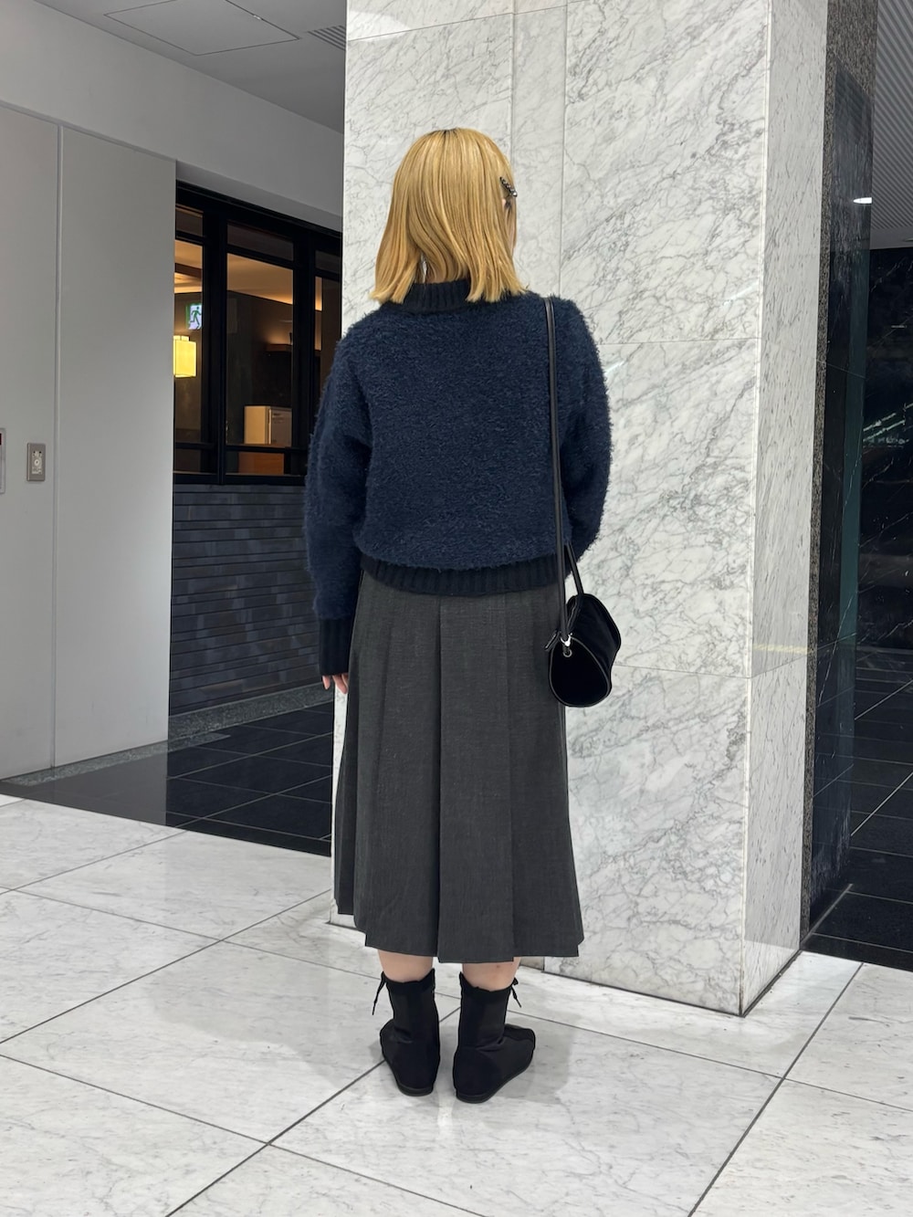 グレー系のスカート、ブルー系のニット/セーター、ブラック系のショルダーバッグを着用したレディースの秋コーディネートの2枚目の写真