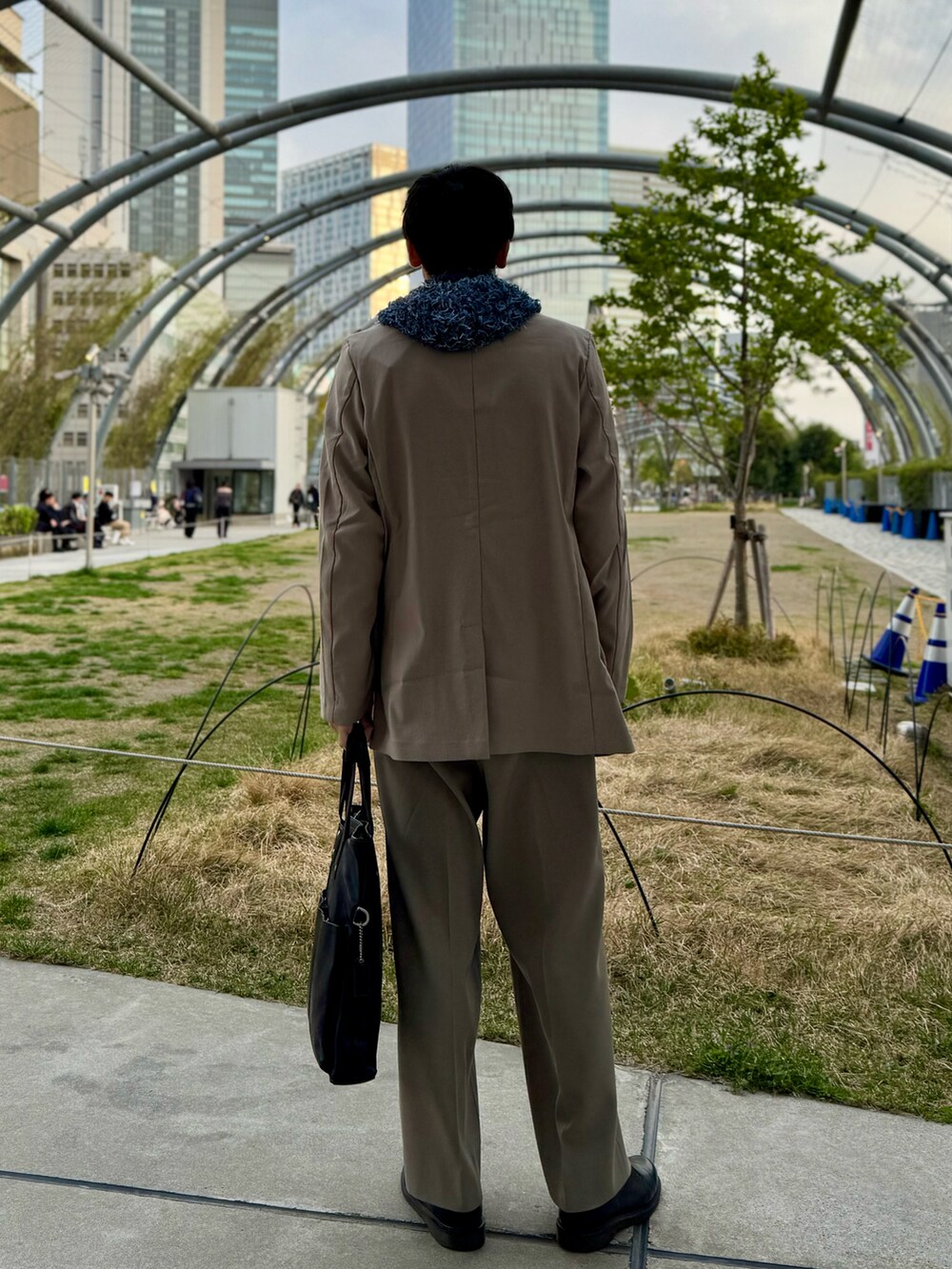 ブルー系のニット/セーター、グレー系のテーラードジャケット、ブラック系のトートバッグを着用したメンズの春コーディネートの2枚目の写真