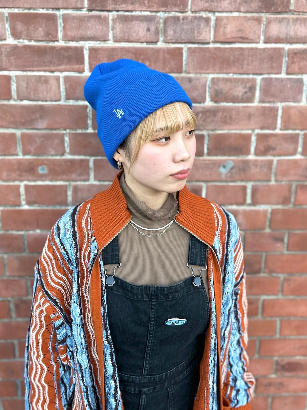 オレンジ系のカーディガン/ボレロ、ブラック系のサロペット/オーバーオール、ブルー系のニットキャップ/ビーニーを着用したレディースの冬コーディネートの2枚目の写真