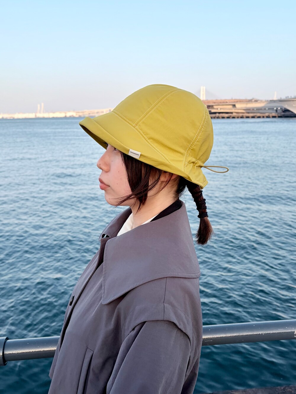 グレー系のトレンチコート、グリーン系のスカート、ブラック系のスニーカーを着用したレディースの冬コーディネートの5枚目の写真