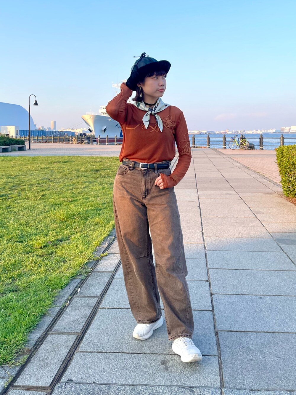 オレンジ系のTシャツ/カットソー、ブラウン系のデニムパンツ、ホワイト系のスニーカーを着用したレディースの秋コーディネートの2枚目の写真