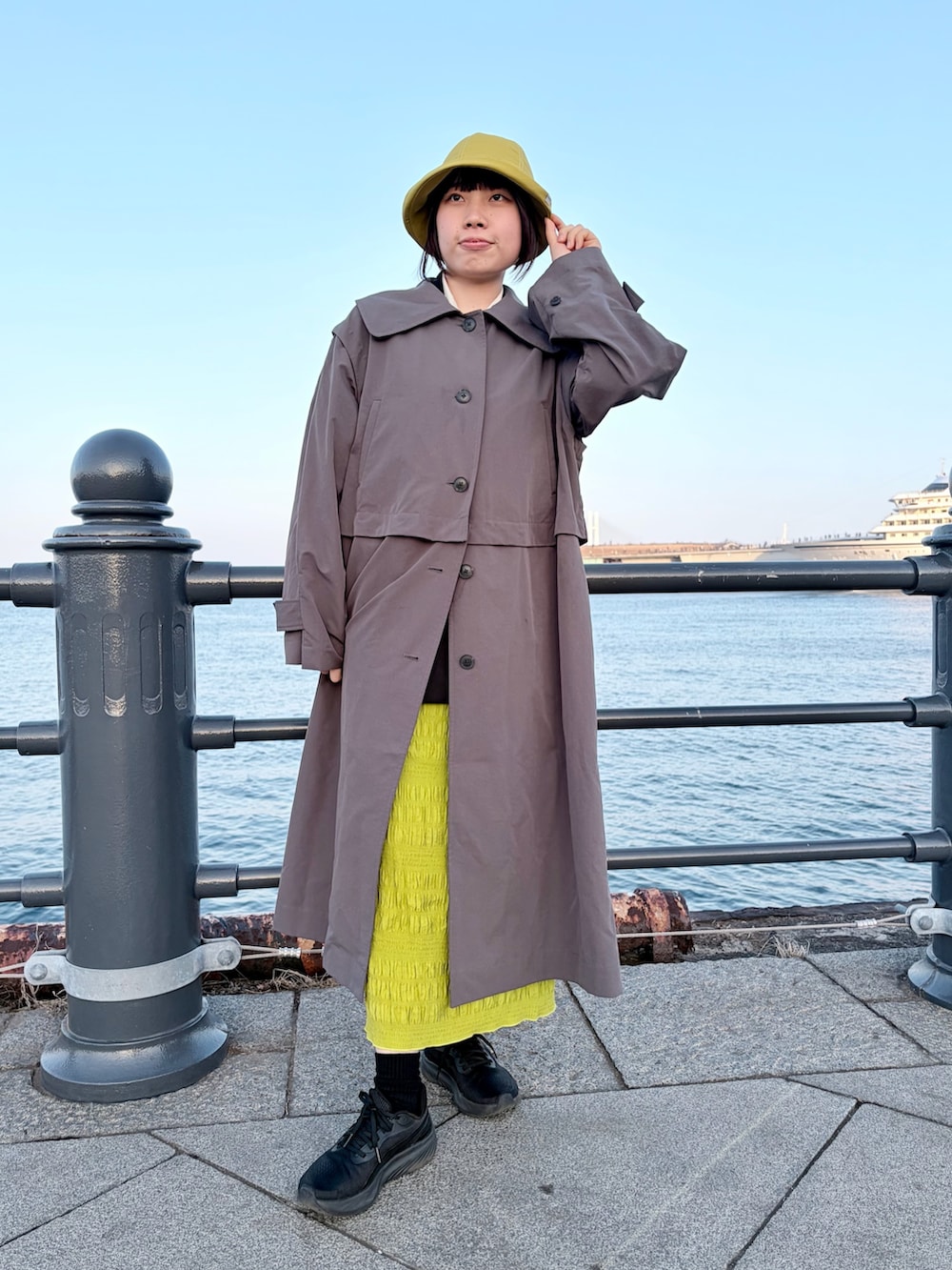 グレー系のトレンチコート、グリーン系のスカート、ブラック系のスニーカーを着用したレディースの冬コーディネートの2枚目の写真