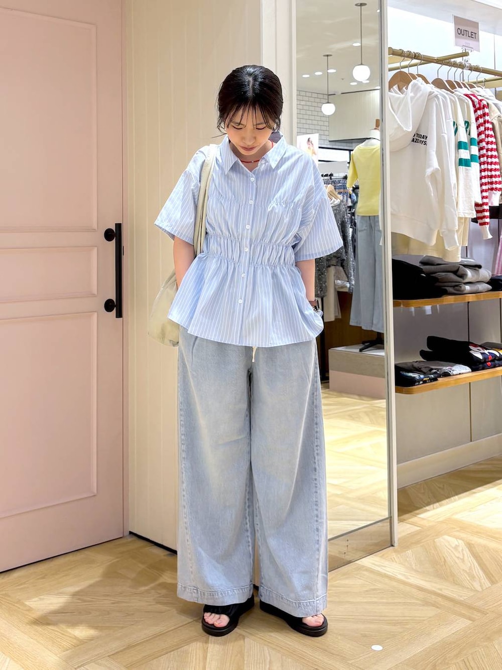 ブルー系のデニムパンツ、ブラック系のサンダル、ホワイト系のトートバッグを着用したレディースの春コーディネートの4枚目の写真