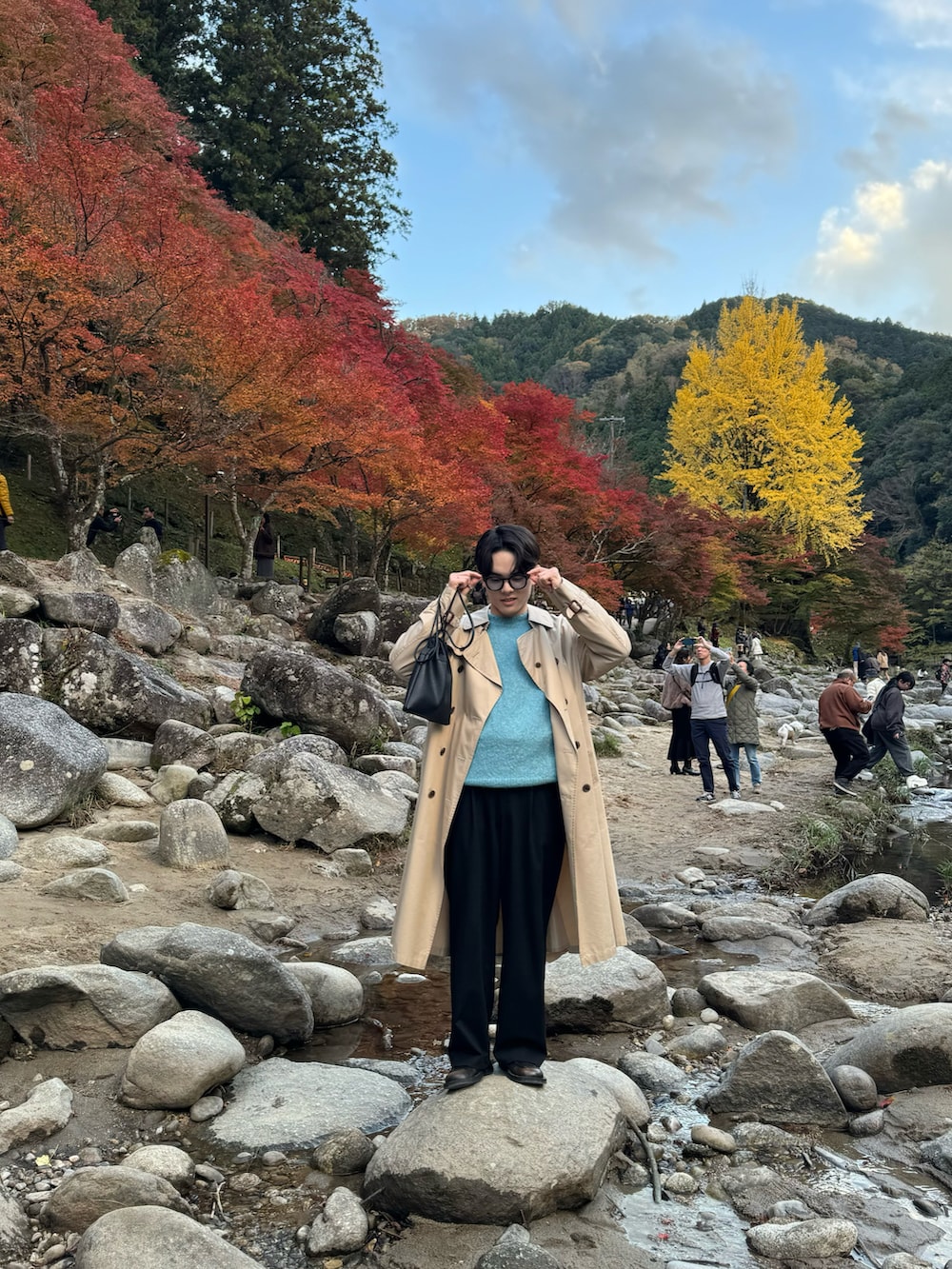 ブルー系のニット/セーター、ベージュ系のトレンチコート、ブラック系のスラックスを着用したメンズの冬コーディネートの2枚目の写真