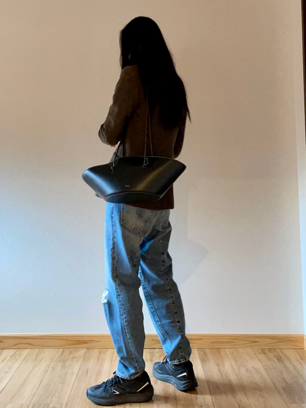 ブラウン系のテーラードジャケット、ブラック系のショルダーバッグ、ブルー系のデニムパンツを着用したレディースの秋コーディネートの4枚目の写真