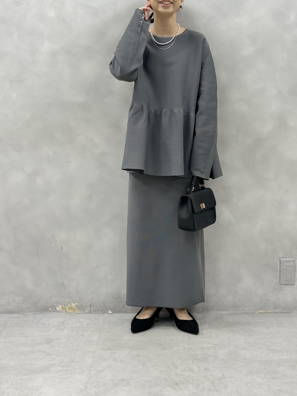 グレー系のニット/セーター、グレー系のスカート、ブラック系のショルダーバッグを着用したレディースの春コーディネートの2枚目の写真