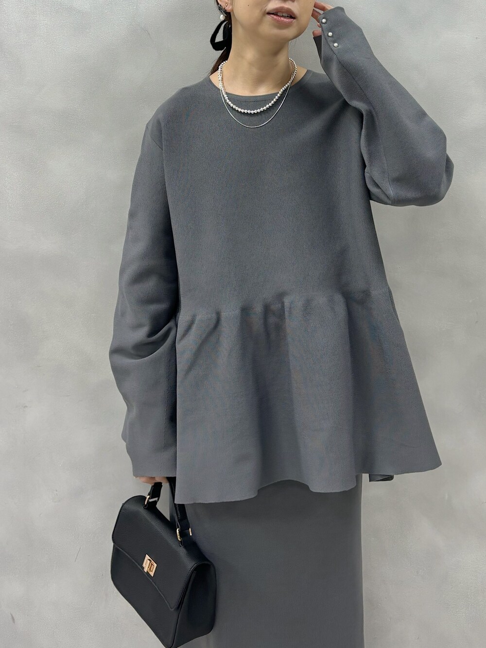 グレー系のニット/セーター、グレー系のスカート、ブラック系のショルダーバッグを着用したレディースの春コーディネートの3枚目の写真