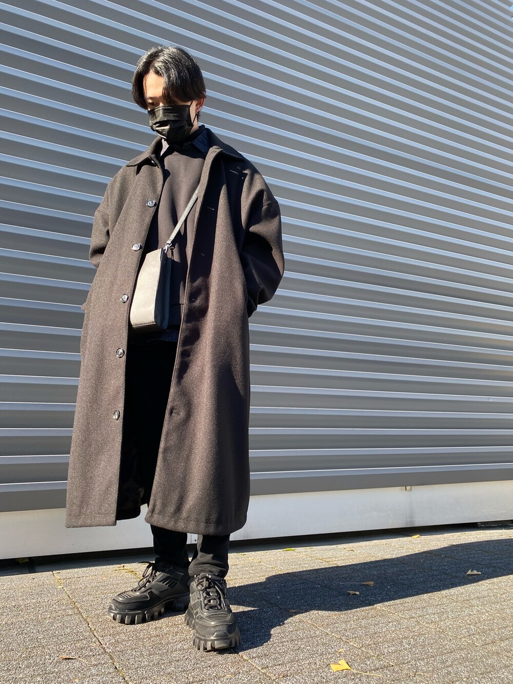 ブラック系のパンツ、ブラック系のステンカラーコート、ブラック系のショルダーバッグを着用したメンズの冬コーディネートの2枚目の写真