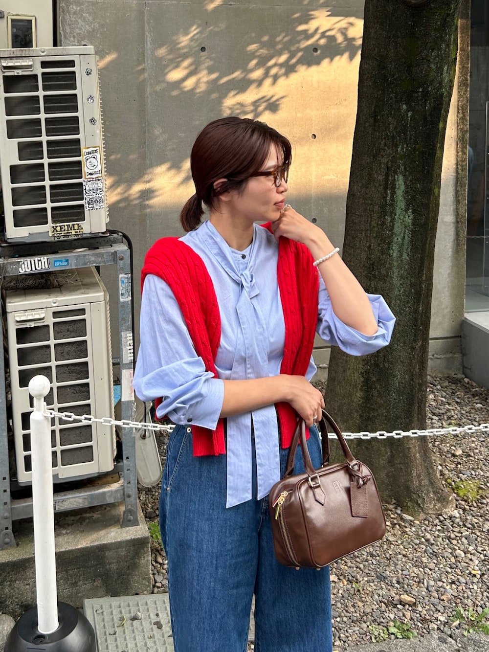 ブルー系のデニムパンツ、ブラウン系のハンドバッグ、レッド系のニット/セーターを着用したレディースの秋コーディネートの3枚目の写真