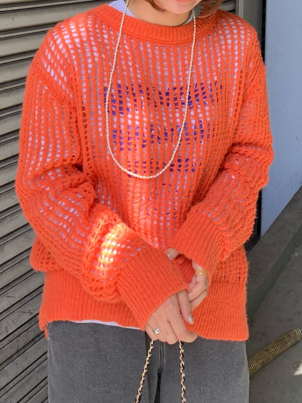 グレー系のデニムパンツ、ブラック系のショルダーバッグ、オレンジ系のニット/セーターを着用したレディースの秋コーディネートの4枚目の写真