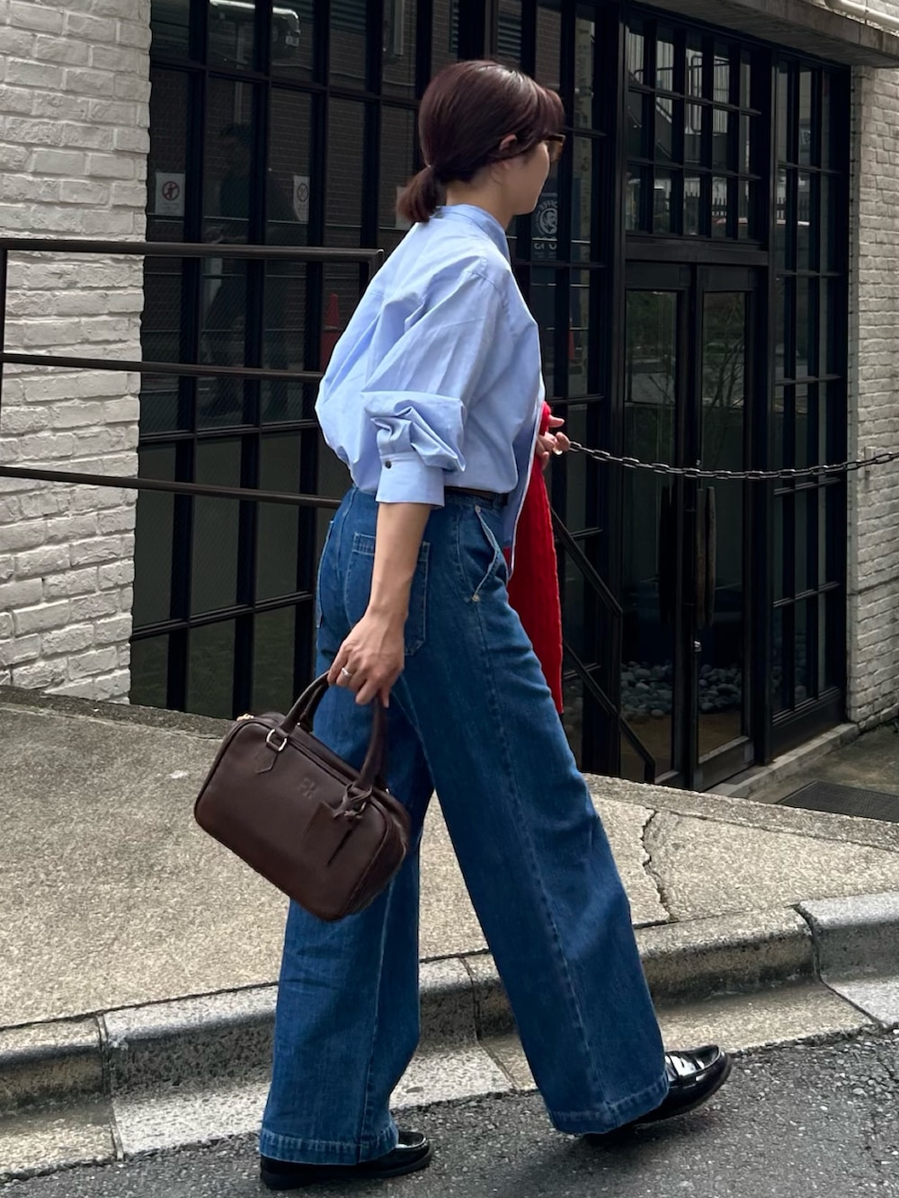 ブルー系のデニムパンツ、ブラウン系のハンドバッグ、レッド系のニット/セーターを着用したレディースの秋コーディネートの4枚目の写真