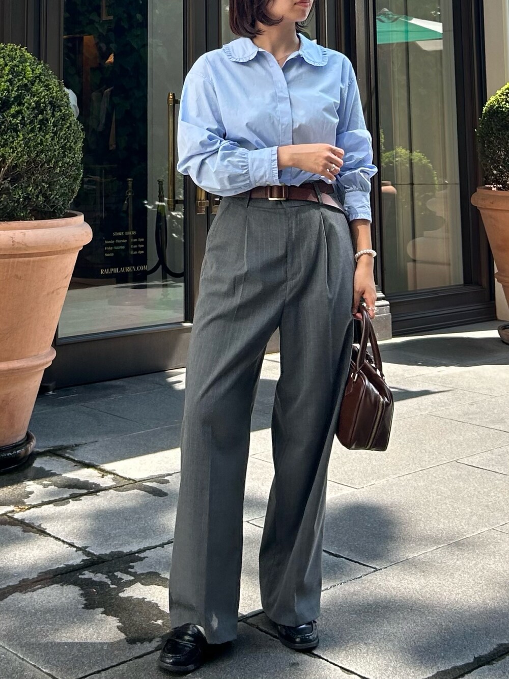 グレー系のスラックス、ブルー系のシャツ/ブラウス、ブラウン系のハンドバッグを着用したレディースの秋コーディネートの2枚目の写真