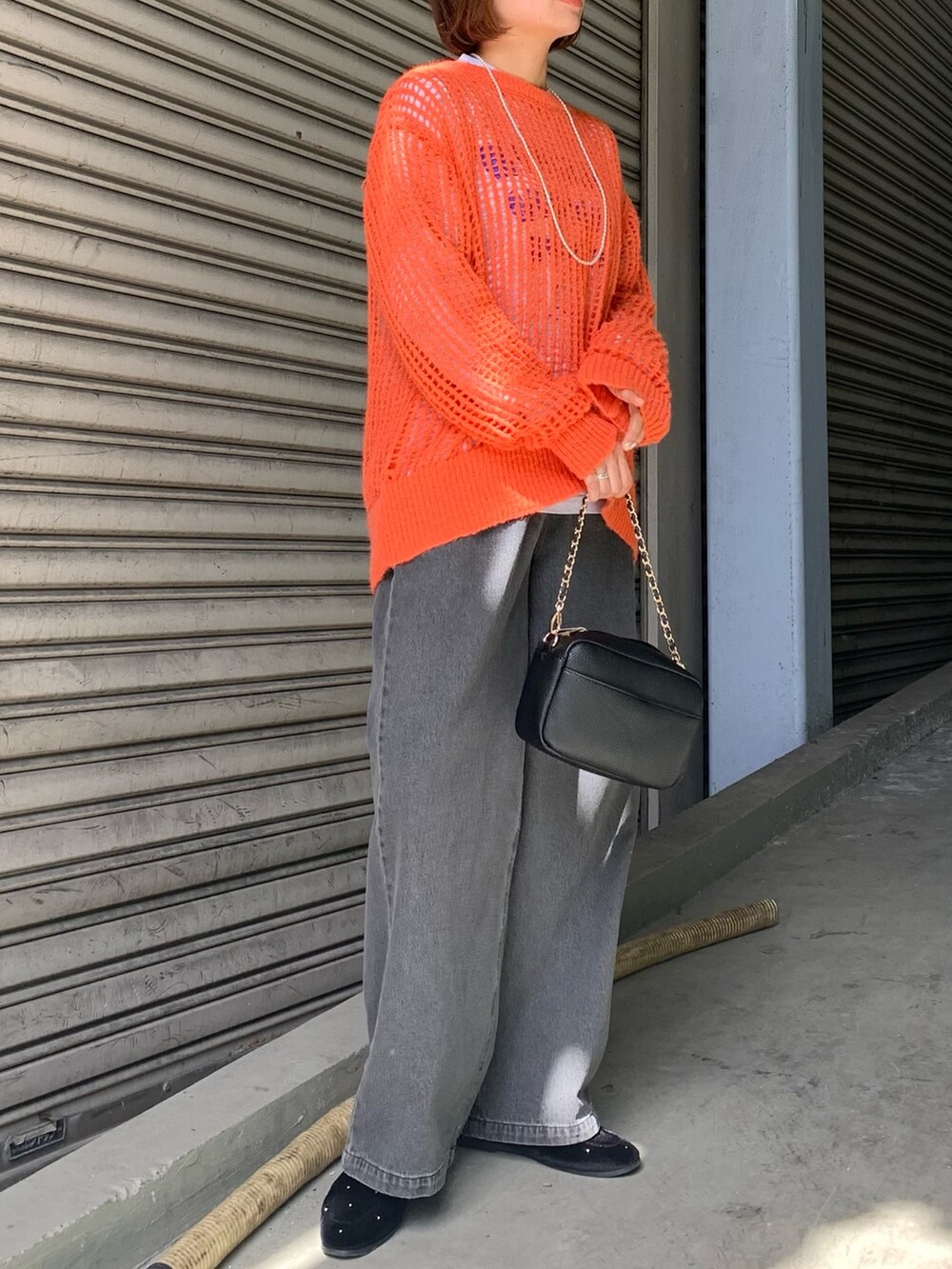 グレー系のデニムパンツ、ブラック系のショルダーバッグ、オレンジ系のニット/セーターを着用したレディースの秋コーディネートの2枚目の写真