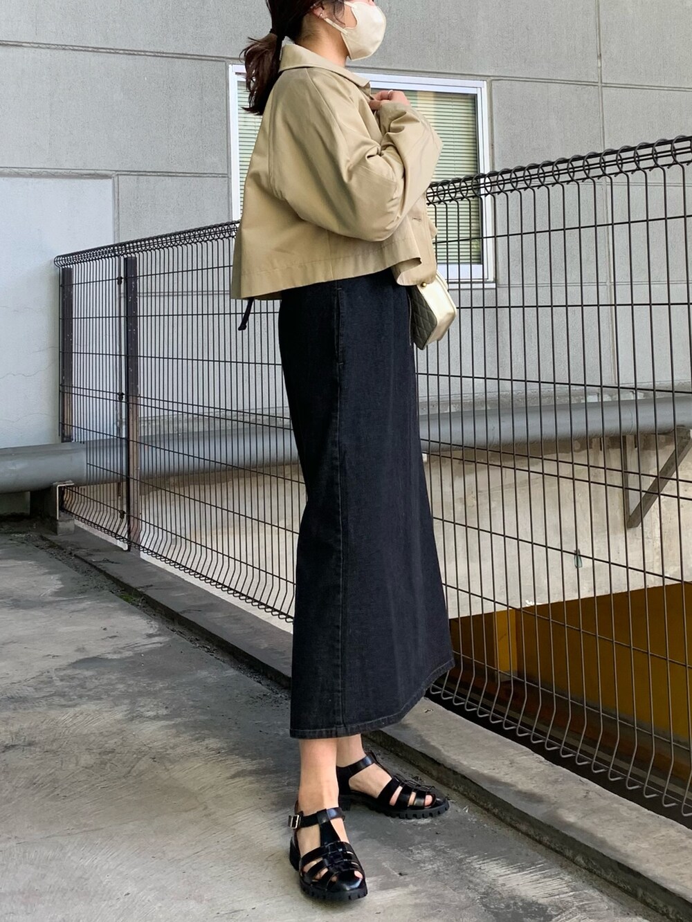 ブラック系のジャンパースカート、ベージュ系のトレンチコート、グリーン系のシャツ/ブラウスを着用したレディースの春コーディネートの2枚目の写真