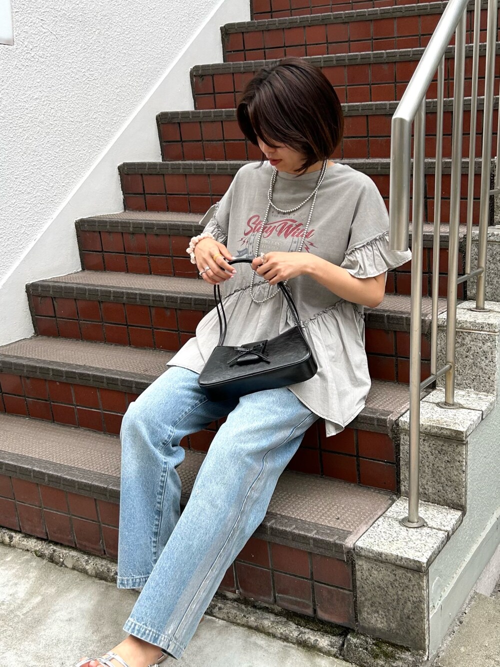 グレー系のTシャツ/カットソー、ブラック系のハンドバッグ、シルバー系のサンダルを着用したレディースの夏コーディネートの4枚目の写真
