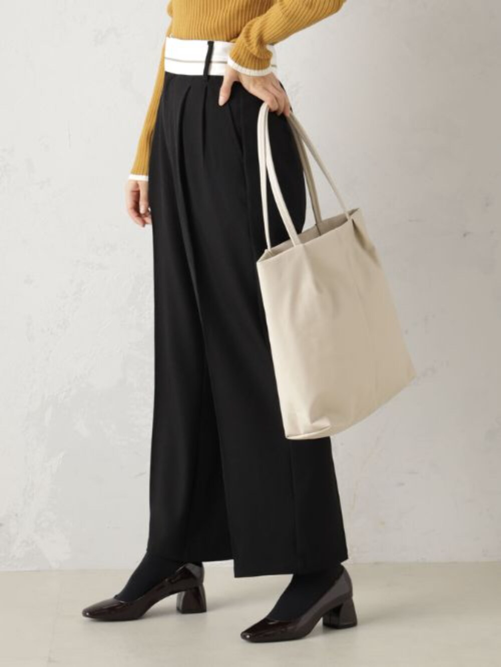 イエロー系のニット/セーター、ブラック系のその他パンツ、ベージュ系のトートバッグを着用したレディースの冬コーディネートの2枚目の写真