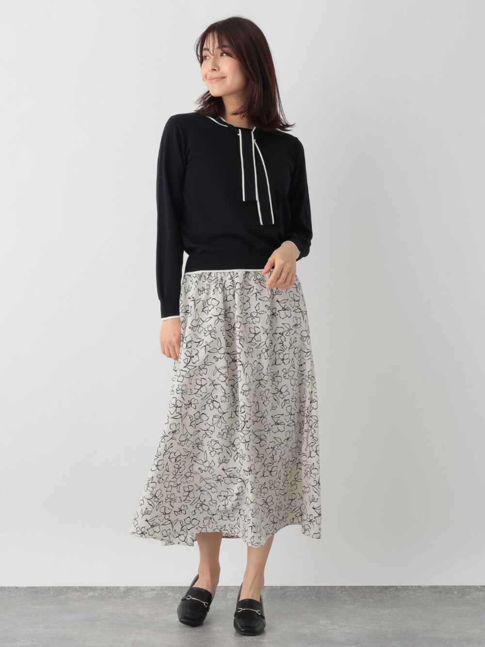 ブラック系のニット/セーター、ベージュ系のスカートを着用したレディースの春コーディネートの2枚目の写真