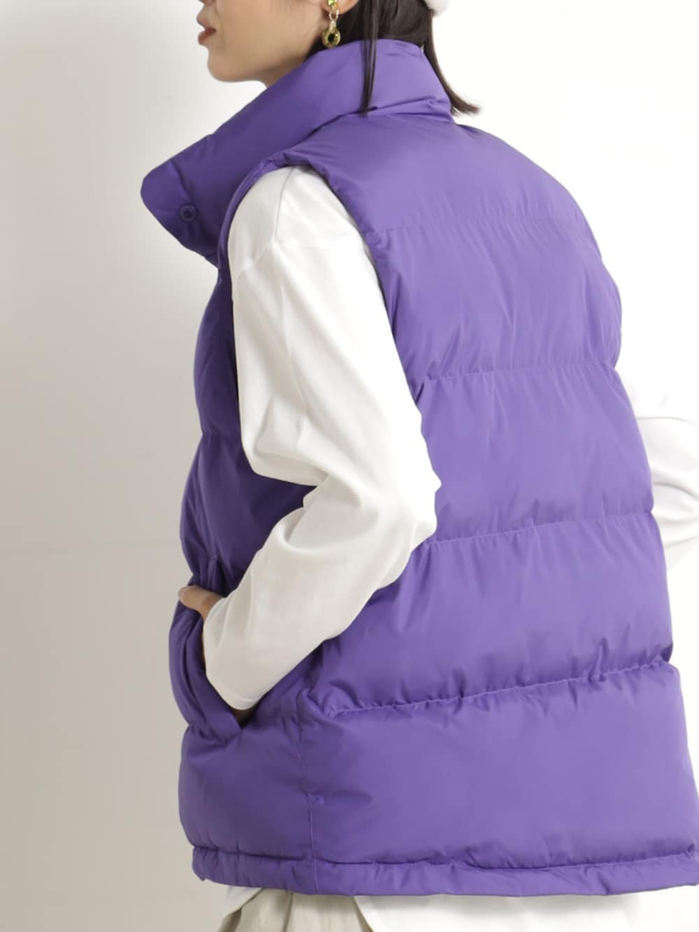 ブラウン系のブーツ、ベージュ系のスカート、パープル系のダウンベストを着用したレディースの冬コーディネートの2枚目の写真