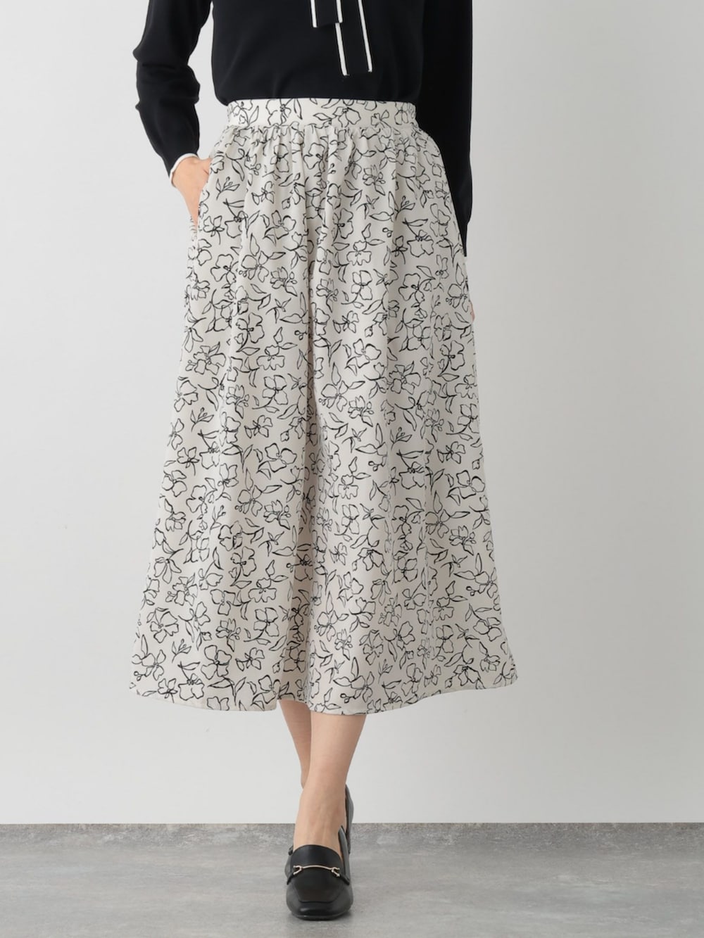 ブラック系のニット/セーター、ベージュ系のスカートを着用したレディースの春コーディネートの2枚目の写真