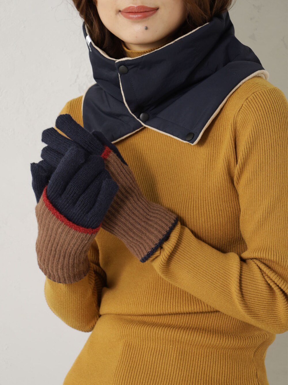 イエロー系のニット/セーター、ブルー系のネックウォーマー/スヌード、ベージュ系の手袋を着用したレディースの冬コーディネートの2枚目の写真