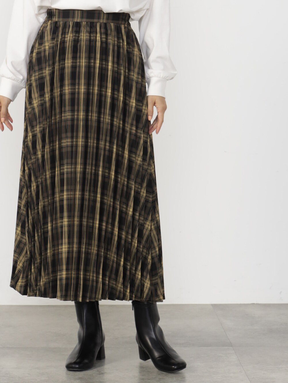 ブラウン系のニット/セーター、ブラウン系のスカート、ブラック系のブーツを着用したレディースの秋コーディネートの2枚目の写真