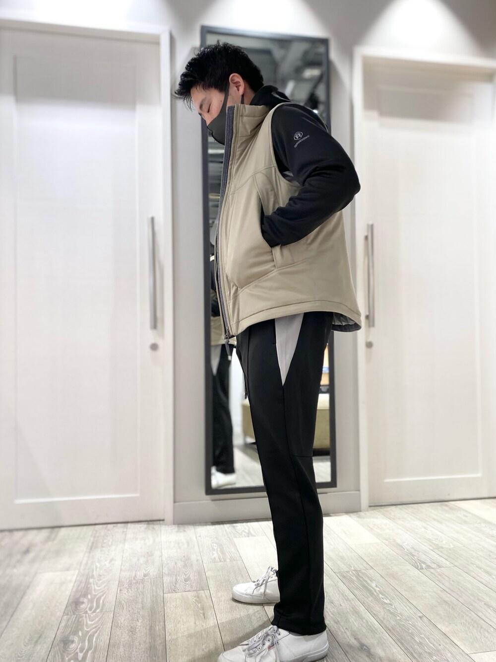 ブラック系のパーカー、ベージュ系のダウンベスト、ブラック系のスラックスを着用したメンズの冬コーディネートの2枚目の写真