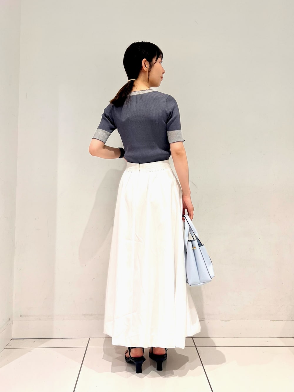 グレー系のニット/セーター、ホワイト系のスカート、ブルー系のトートバッグを着用したレディースの夏コーディネートの2枚目の写真