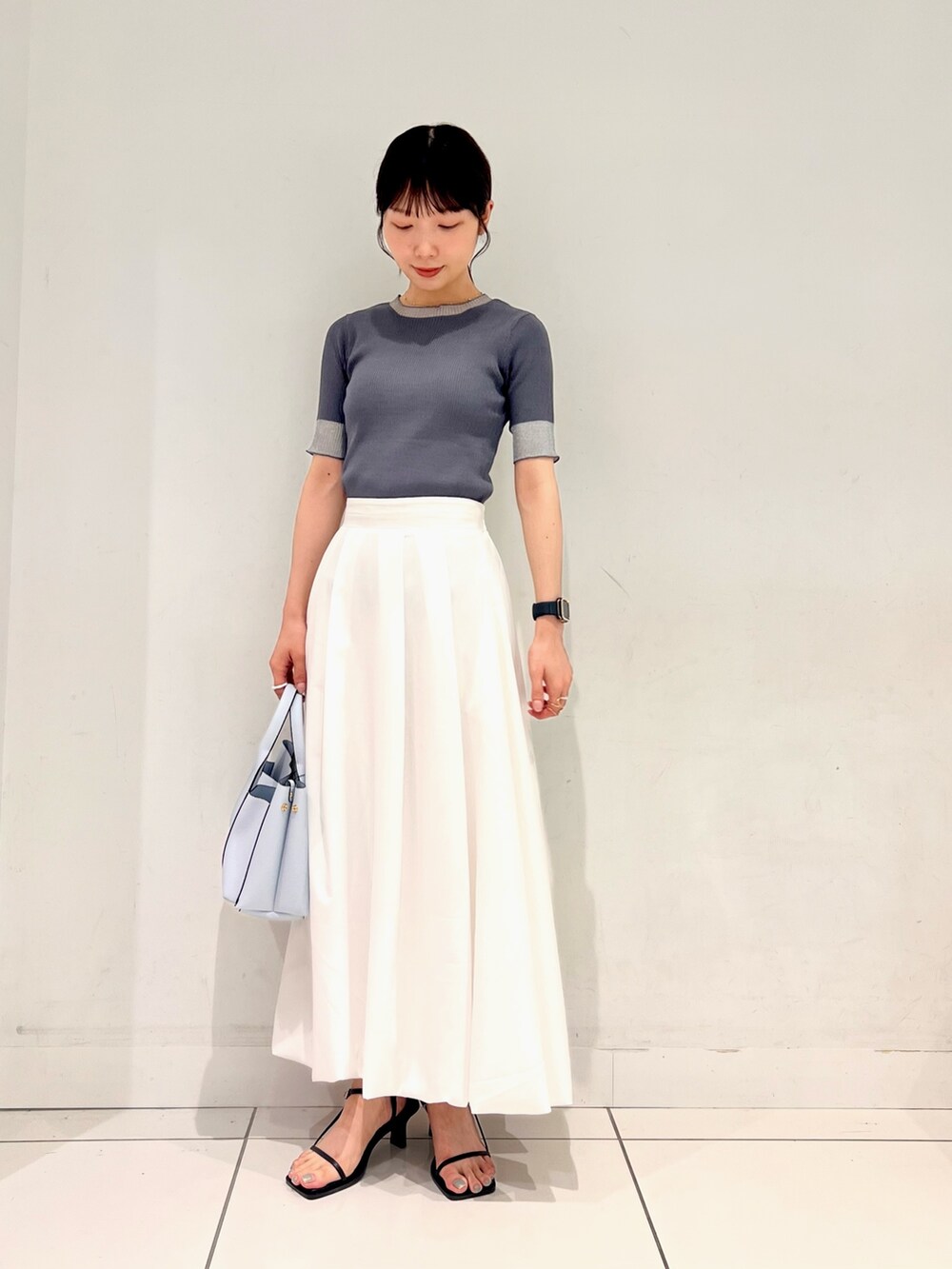 グレー系のニット/セーター、ホワイト系のスカート、ブルー系のトートバッグを着用したレディースの夏コーディネートの3枚目の写真