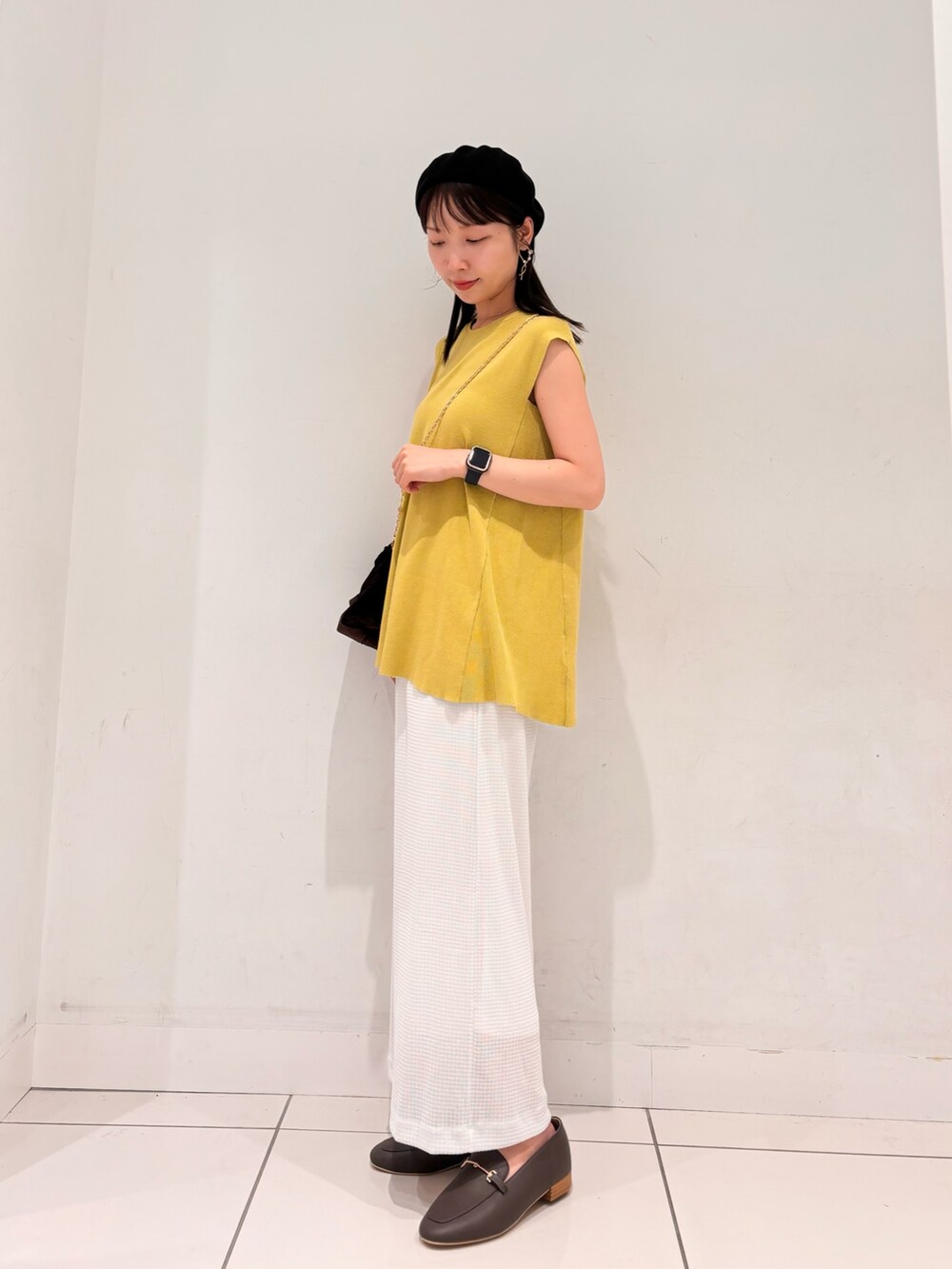イエロー系のニット/セーター、ブラウン系のハンドバッグ、ホワイト系のスカートを着用したレディースの夏コーディネートの2枚目の写真
