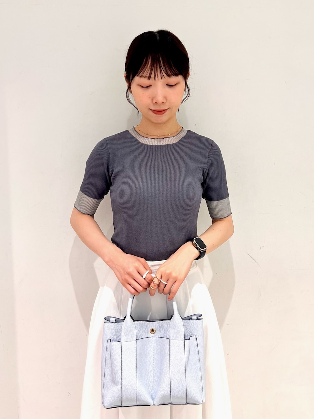 グレー系のニット/セーター、ホワイト系のスカート、ブルー系のトートバッグを着用したレディースの夏コーディネートの4枚目の写真
