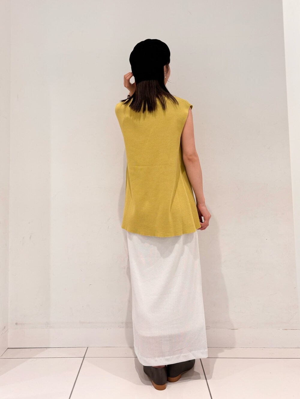 イエロー系のニット/セーター、ブラウン系のハンドバッグ、ホワイト系のスカートを着用したレディースの夏コーディネートの3枚目の写真